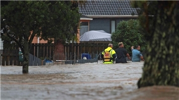 Menschen waten durch das Hochwasser einer vollkommen überschwemmten Straße in Auckland.