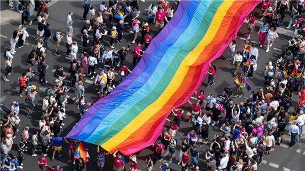 Hunderttausende feiern friedlichen CSD in Berlin Menschen ziehen mit einer überdimensionalen Regenbogenfahne durch die Stadt.