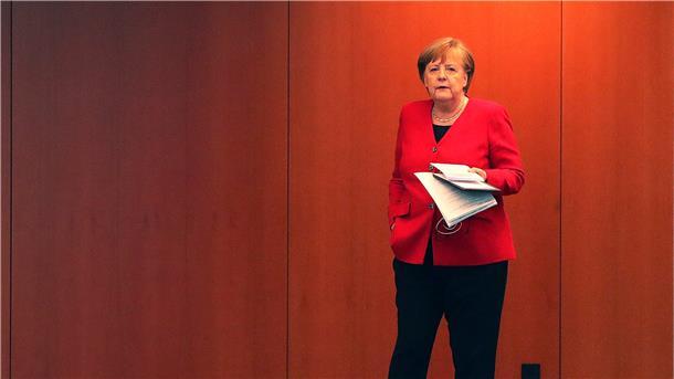 Angela Merkel mit einer Hand in der Hosentasche und in der anderen Hand Papier.