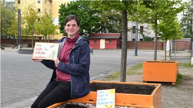 Miriam Gieseking, Leiterin der Quartiersmeisterei Lehe, präsentiert zwei der Schilder, die die Pflanzkästen auf dem Leher Pausenhof vor Vandalismus schützen sollen.