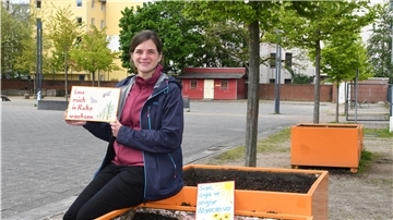 Miriam Gieseking, Leiterin der Quartiersmeisterei Lehe, präsentiert zwei der Schilder, die die Pflanzkästen auf dem Leher Pausenhof vor Vandalismus schützen sollen.