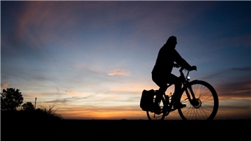 Ein Mann fährt mit einem Fahrrad kurz nach Sonnenaufgang über einen Feldweg.
