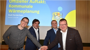 Vier Männer stehen nebeneinander und drücken einen symbolischen roten Knopf.