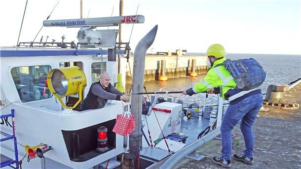 Mit einer langen Stange reicht Inga-Kristin Thom von der Seemannsmission in Cuxhaven coronagerecht Tüten mit Weihnachtsgeschenken an Bord des Mehrzweckfrachters Annika B., der unter zyprischer Flagge fährt.