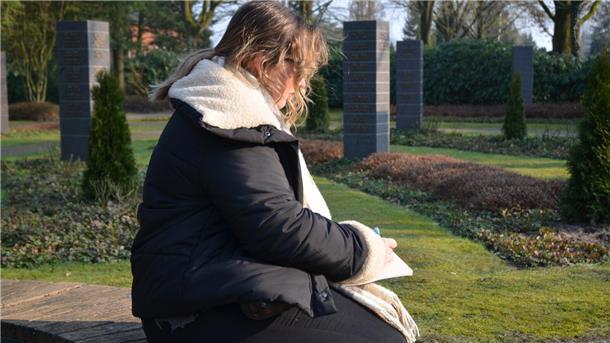 Trauer in Zeven: Josephines Opa lebt in Geschichten weiter Eine junge Frau sitzt auf einem Friedhof und schreibt einen Text auf einen Block.