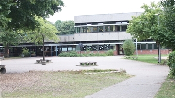 Blick auf den Schulhof und das Gebäude der Grundschule Beverstedt mit Bäumen im Vordergrund. An den Fenstern hängen bunte Girlanden und Papierdekorationen.