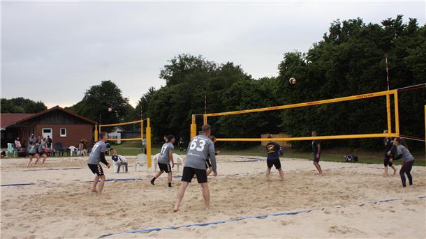 Eine Gruppe Sportler spielt auf zwei nebeneinander liegenden Sandplätzen Beachvolleyball