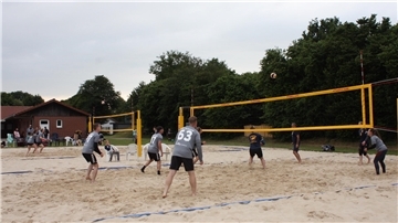 Eine Gruppe Sportler spielt auf zwei nebeneinander liegenden Sandplätzen Beachvolleyball