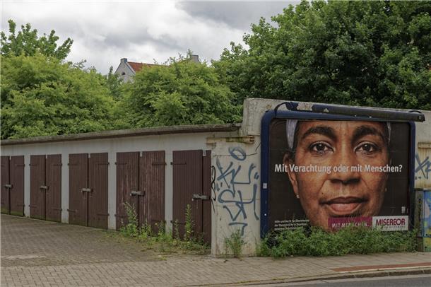 Wie Fotograf Thomas Damson Bremerhavens "große Wunde" Lehe sieht "Mit Verachtung oder mit Menschen?" Ein Plakat von Misereor an einem Garagenhof in Lehe, das sinnbildlich für das Kernthema im Blog von Fotograf Thomas Damson steht.