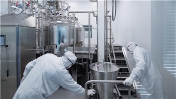Mitarbeiter eines Pharmaunternehmens arbeiten in einem Reinraum an einer Gelmischanlage.