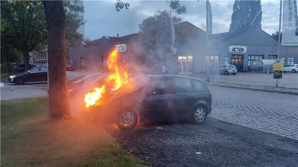 Ein brennendes Fahrzeug steht auf einem Parkplatz.