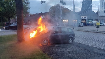Ein brennendes Fahrzeug steht auf einem Parkplatz.