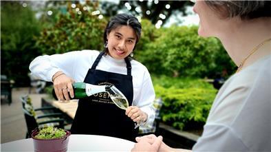 Mitten in der Corona-Krise hat sich die 19-Jährige Nilufar Namazove entschieden, eine Ausbildung im Restaurant des Romantik Hotels Bösehof zu machen. Zur Übung serviert sie ihrer Chefin Andrea Roming Sekt.