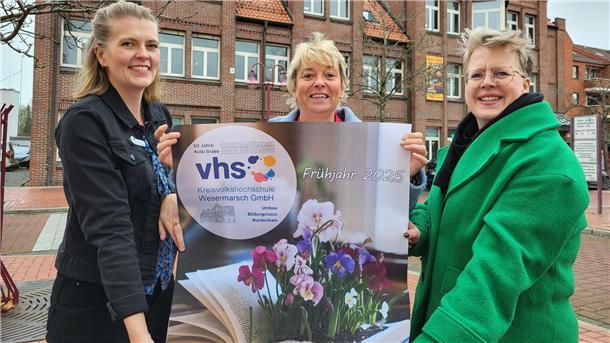 Drei Frauen präsentieren stolz ein Plakat und lächeln in die Kamera. 