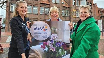 Drei Frauen präsentieren stolz ein Plakat und lächeln in die Kamera. 