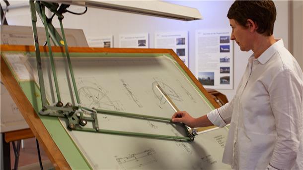 Museumsleiterin Dr. Anja Dörfer steht an einem Original-Zeichentisch, an dem einst Flugzeugteile für die VFW 614 konstruiert worden sind.