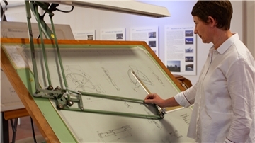 Museumsleiterin Dr. Anja Dörfer steht an einem Original-Zeichentisch, an dem einst Flugzeugteile für die VFW 614 konstruiert worden sind.