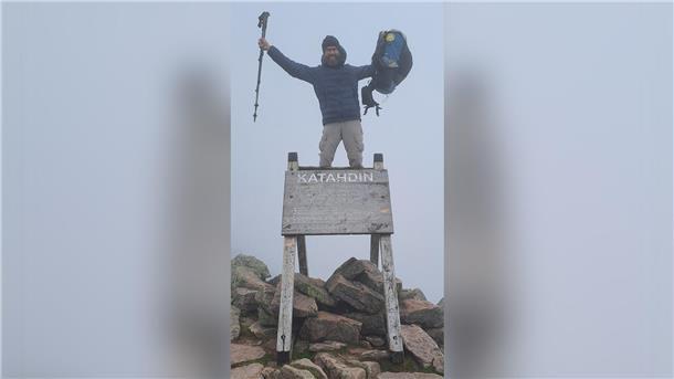 Ein Mann posiert mit Rucksack und Wanderstöcken auf dem Gipfel des Mount Katahdin.