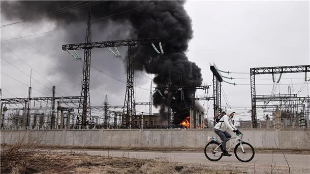 Krieg gegen die Ukraine: So ist die Lage Nach einem russischen Angriff fährt ein Mann mit seinem Rad an einem brennenden Elektrizitätswerk in Charkiw vorbei.