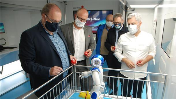 Nach kurzer Programmierung ist der humanoide Roboter Nao auf dem Weg, um Geestlands Bürgermeister Thorsten Krüger (links) den Stoffbären in die Hand zu drücken. Aufmerksame Beobachter sind (von links) Rafael Platek, Horst Lüdtke, Uwe Nixdorf und Engin Öztürk, Projektleiter im Sciene Truck. Foto Schoener