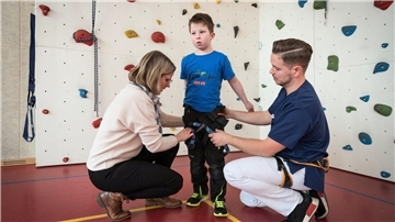 Der neunjährige Helge wird für seinen Ausflug an die Kletterwand von seiner Mutter Emely Peters und von Physiotherapeut Philip Ewert abgesichert.
