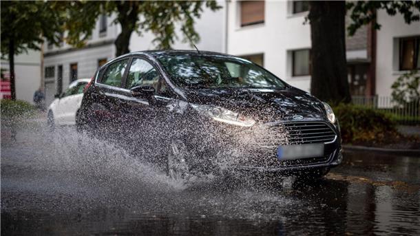 Nach starken Regenfällen am Dienstagmorgen fährt ein Auto durch eine große Pfütze in Duisburg.