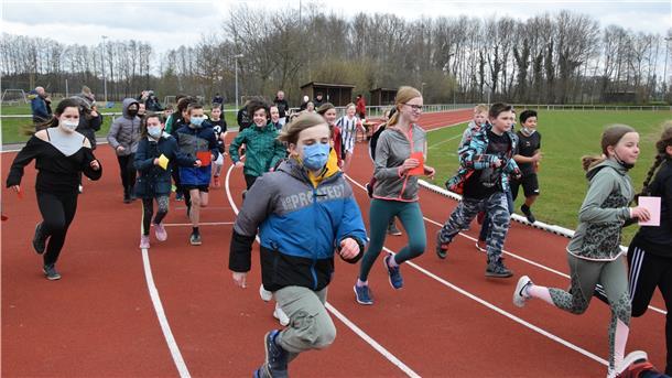 Mehrere Kinder laufen über die Bahn eines Sportplatzes.