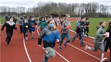 Mehrere Kinder laufen über die Bahn eines Sportplatzes.