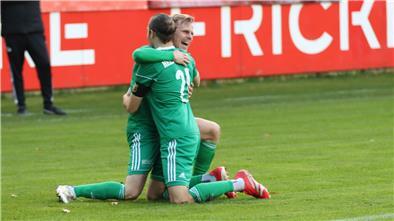 Zwei Männer knien auf dem Fußballrasen und liegen sich lachend in den Armen.