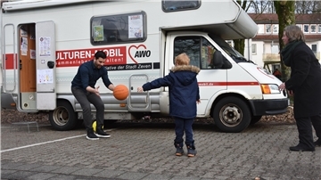 Zwei Erwachsene und ein Kind spielen Ball vor einem Wohnmobil.