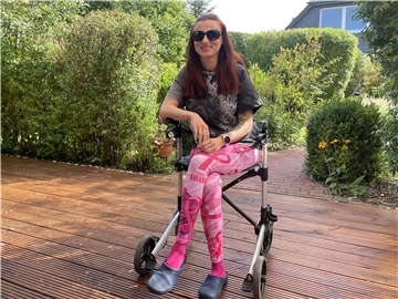 Junge Frau sitzt auf einem Rollator auf einer Terrasse