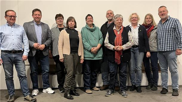 Zehn Frauen und Männer stehen nebeneinander vor einer Wand.