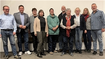 Zehn Frauen und Männer stehen nebeneinander vor einer Wand.