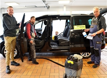 Drei Männer in einer Auto-Werkstatt. 