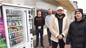 Vier Männer stehen neben einem Automaten mit Getränken und Snacks.