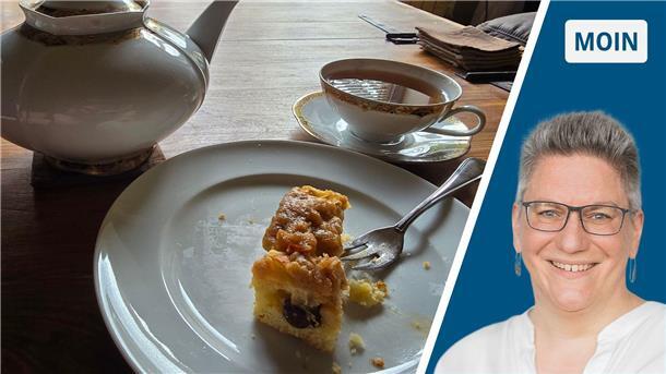 Ein Stück Kuchen liegt auf einem Teller auf einem Wohnzimmertisch. Daneben steht eine Teekanne und eine volle Teetasse.