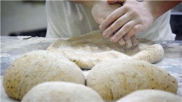 Hände eines Bäckers formen einen Teig zu Brot und Brötchen. 