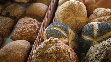 Verschiedene mit Körnern bedeckte Brötchen liegen in der Auslage eines Bäckers