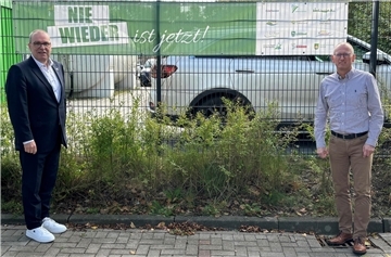 Zwei Männer stehen vor einem Banner, auf dem „Nie wieder ist jetzt!" zu lesen ist. 