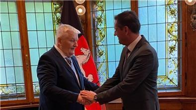 Zwei Herren im Anzug reichen sich freundschaftlich die Hände. Sie stehen in einem repräsentativen Raum, im Hintergrund eine Flagge mit Nidersachsenpferd.