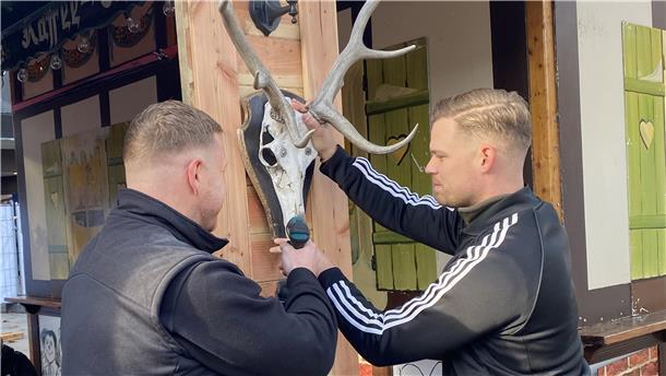 Zwei Männer schrauben ein Hirschgeweih an eine Wand.