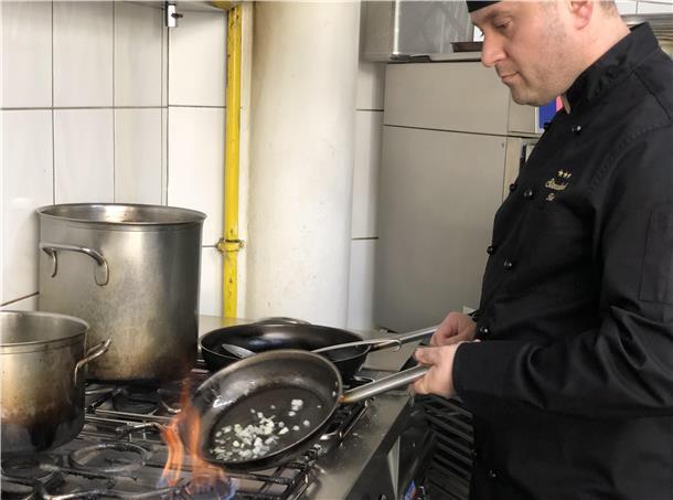 Der Koch des Scala brät Zwiebeln in einer Pfanne an.