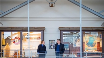 Oben an der Decke hängt die Klanginstallation in Form einer Schiffsglocke, die den Wellengang akustisch überträgt. Künstlerin Kira Keune übergibt das Kunstwerk an Kai Kähler, Leiter des Historischne Museums.