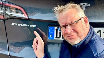 Ein Mann zeigt auf einen Aufkleber auf seinem Auto. Olaf Michalowski mag seinen Tesla, aber nicht Elon Musk.