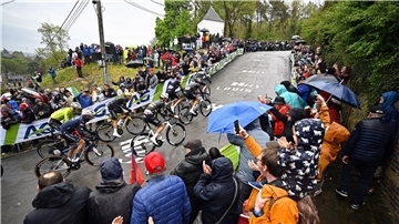 Olympiasieger Remco Evenepoel (M) mit goldenem Helm an der Mauer von Huy. Rechts neben ihm Tadej Pogacar.