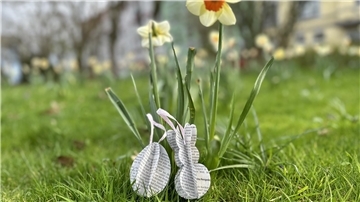 Ein gebasteltes Osterei und ein Hase aus Zeitungspapier auf einer Wiese.
