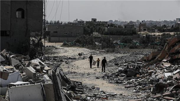 Palästinenser gehen neben zerstörten Wohngebäuden im Lager Nuseirat im zentralen Gazastreifen entlang.