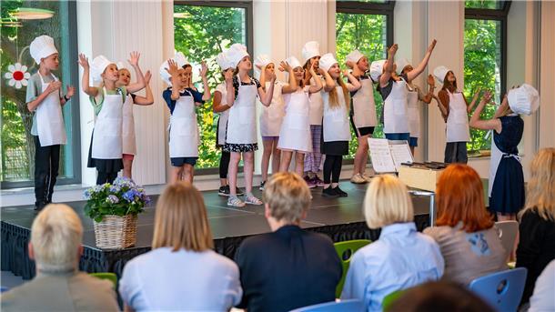 Viertklässler in Schürzen und Kochhüten führen einen Küchen-Rap auf 