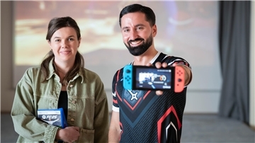 Eine Frau und ein Mann stehen nebeneinander. Der Mann hält ein Nintendo-Switch-Handheld in die Kamera, die Frau trägt zwei Spielhüllen im Arm.