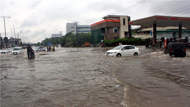Pendler fahren in Lahore eine überschwemmte Straße entlang.